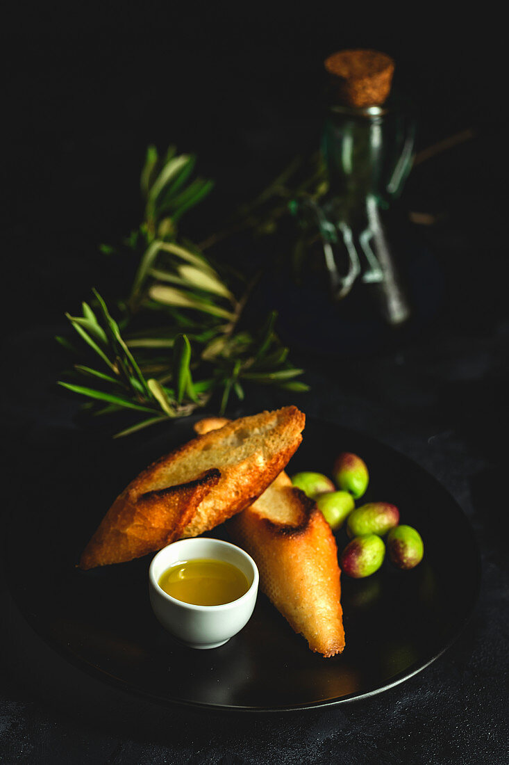 Fresh Spanish extra virgin olive oil with olives and old olive branch on dark background Healthy food Mediterranean diet. Vegan. Vegetarian. Toasted bread