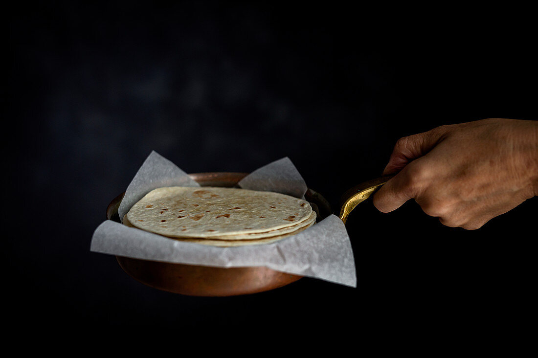 Hand hält Pfanne mit gestapelten Tortillas