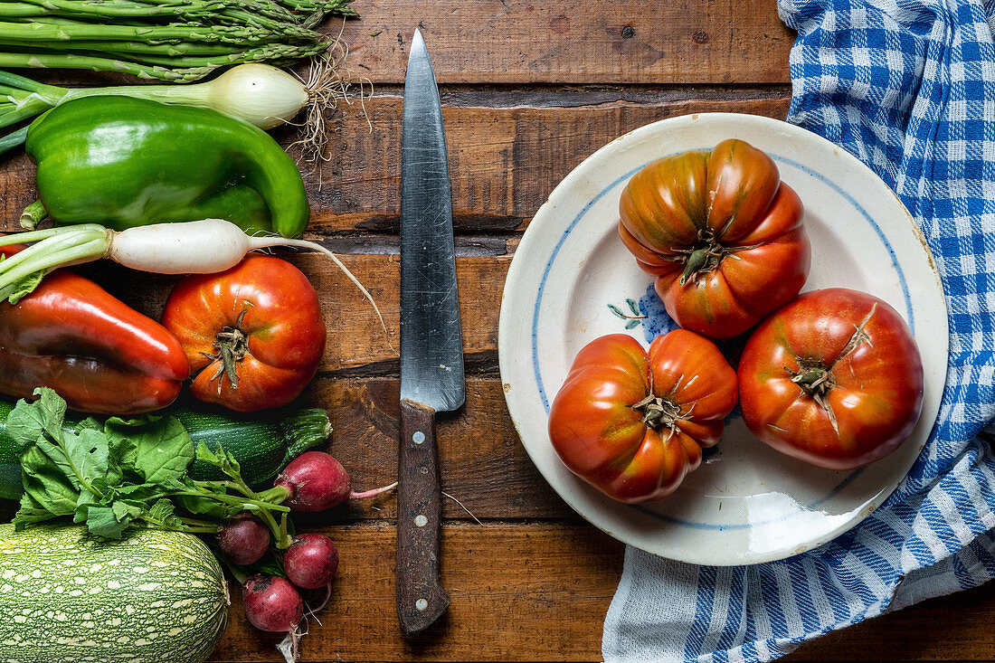 Fresh organic vegetables on a dark wooden table with tomatoes in a bowl and a knife