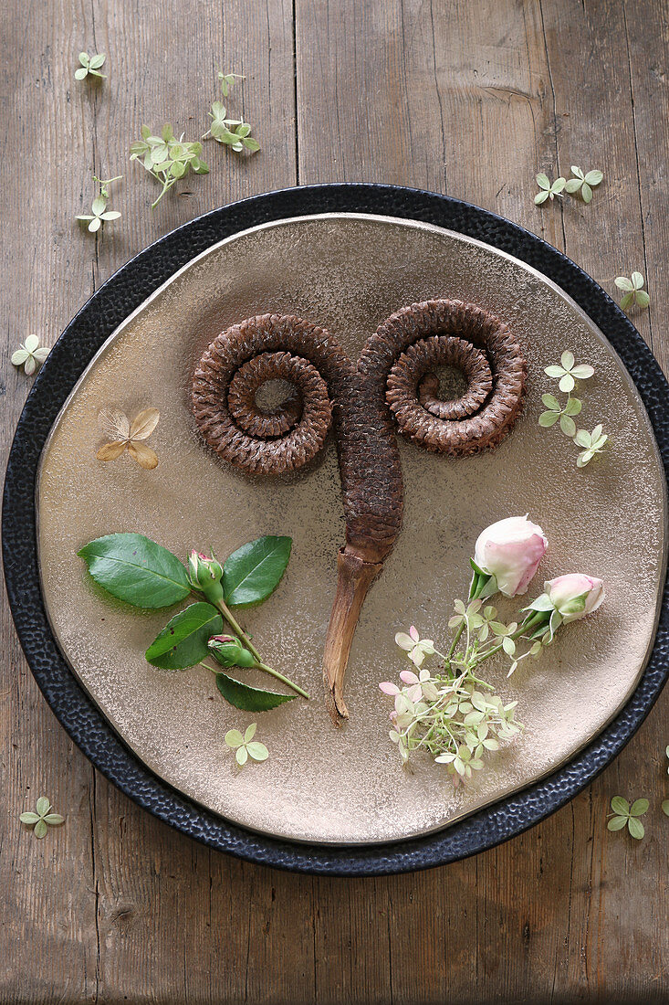 Golden plate decorated with roses, hydrangea florets and pine cone curled into horns