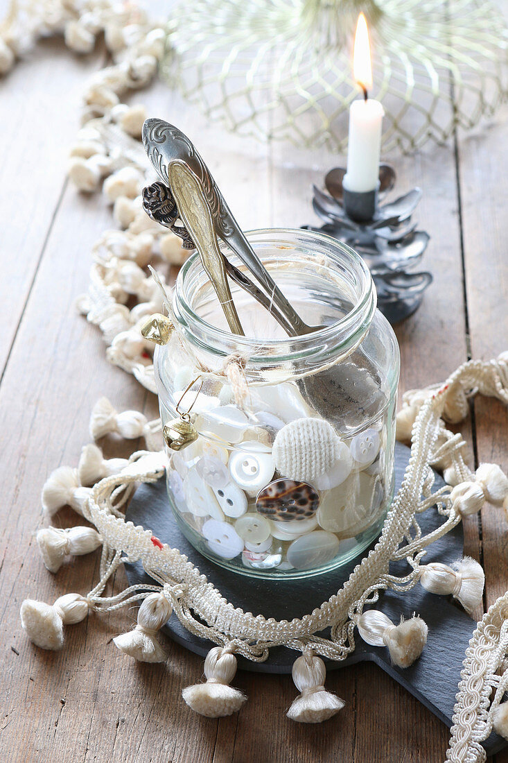 Collection of buttons and antique spoons in jar surrounded by tasselled trim