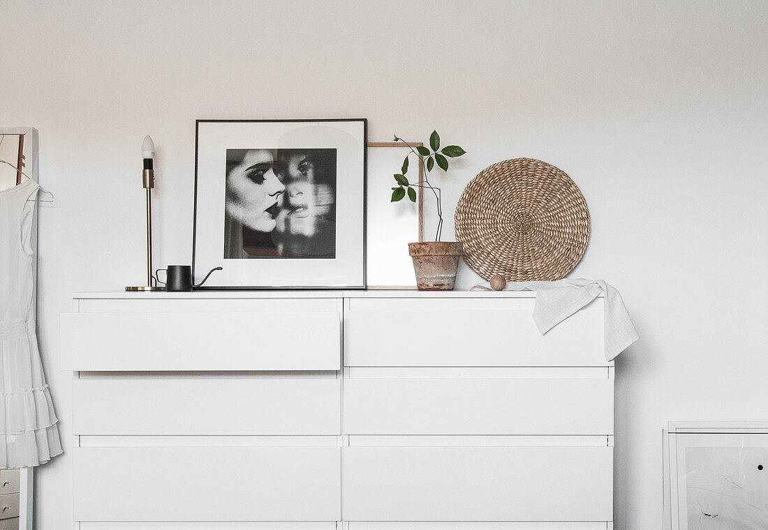 Black-and-whit photo, table lamp and houseplant on white chest of drawers