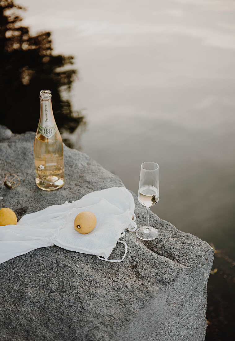 Bottle and glass of sparkling wine on rocky lake shore