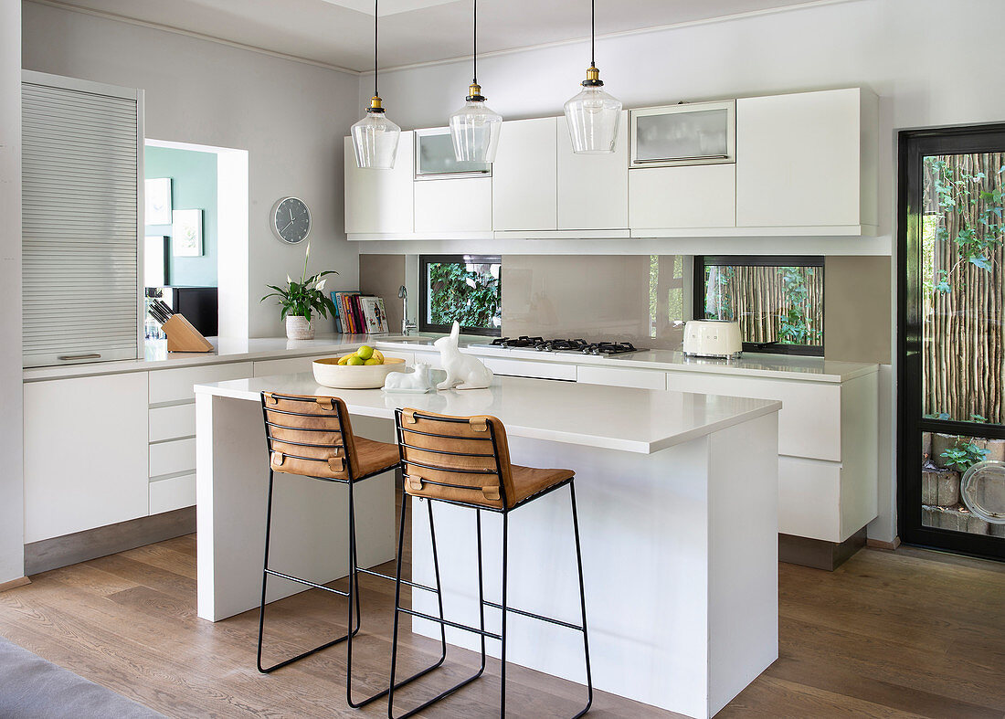 Barstools at counter in modern, white, open-plan kitchen