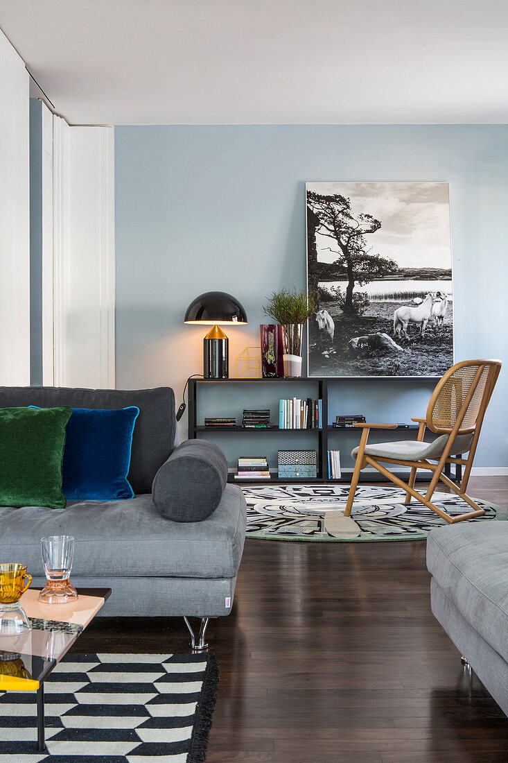 Sofa mit geometrisch gemustertem Teppich und Leseecke mit niedrigem Regal vor blauer Wand