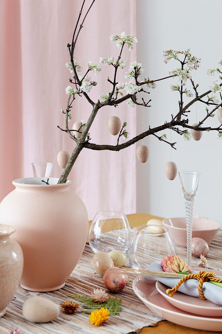 Blütenzweig mit Holzeiern in der Vase auf gedecktem Ostertisch in Rosa