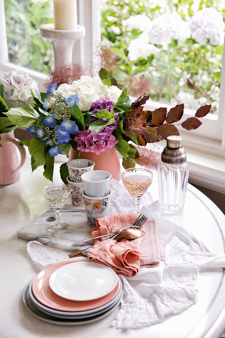 Gedeckter Tisch mit Geschirr, Wein und Blumen vor dem Fenster