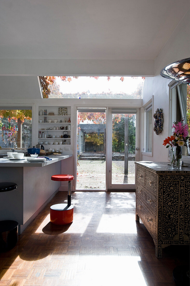 Chest of drawers inlaid with mother-of-pearl, counter and red stool in open-plan kitchen