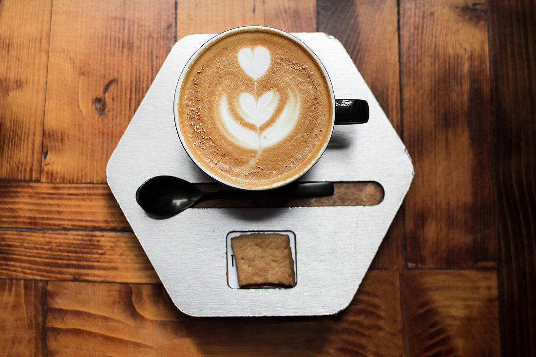 Cappuccino mit Milchschaumherz auf sechseckigem Teller