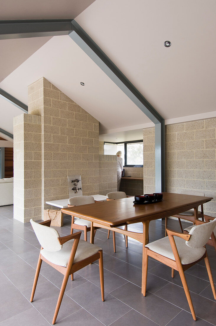 Dining table and upholstered chairs in interior with gable roof and exposed steel beams