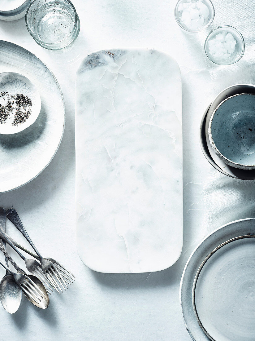 White dishes, glasses, cutlery and a marble platter on a table