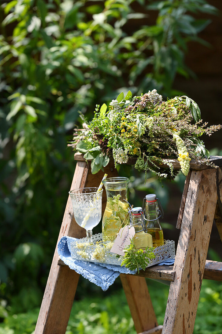 A bunch of summer medicinal herbs and meadowsweet syrup on a wooden ladder