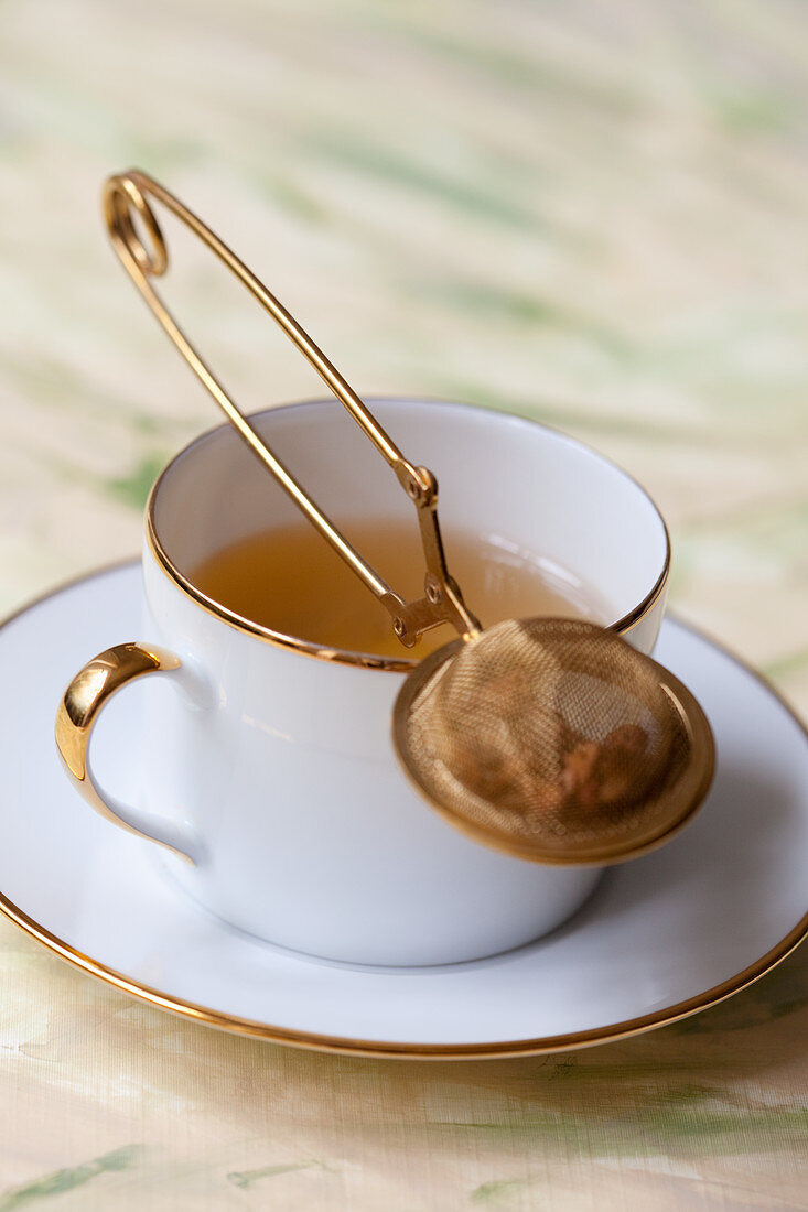 Goldrand-Tasse mit Tee und Teesieb