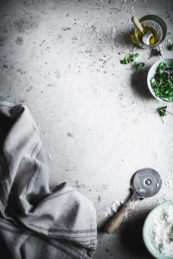 A pizza cutter, flour, cress and olive oil