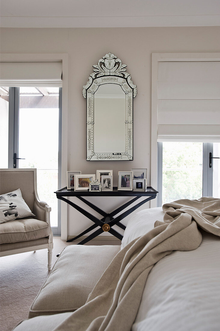 Mirror on wall and pictures on black tray table in beige bedroom