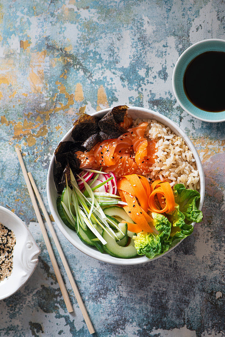 Sushi buddha bowl with salmon, brown sushi rice, nori nori, cucumber, radish, carrot and spring onion