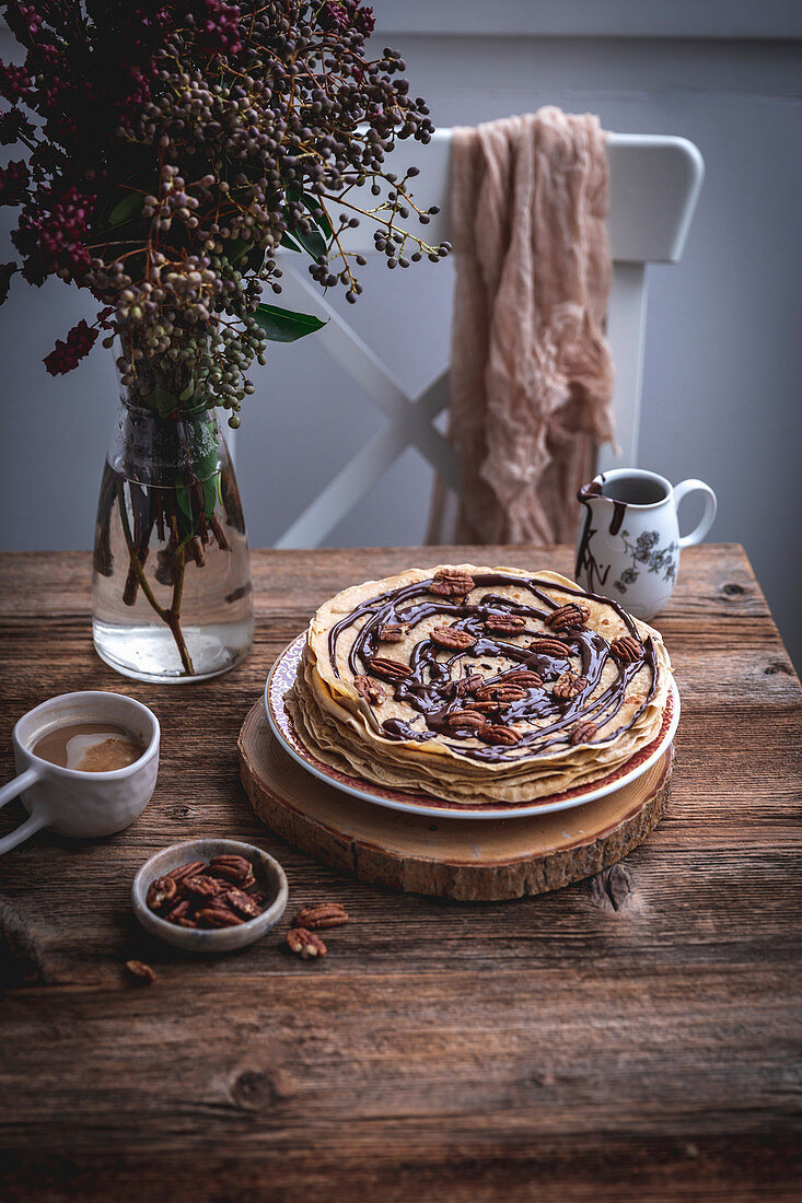 Stack of crepes with melted dark chocolate and pecans and a cup of coffee on a rustic wooden table