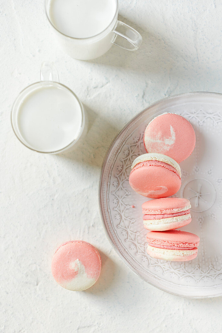 Overhead image of a plate of pink and white macarons with 2 glasses of milk
