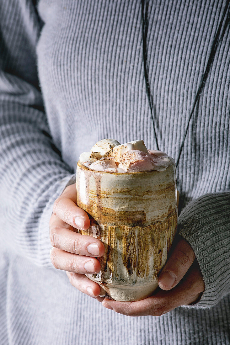 Frau hält ein Glas heiße Schokolade mit Sahne und Marshmallows