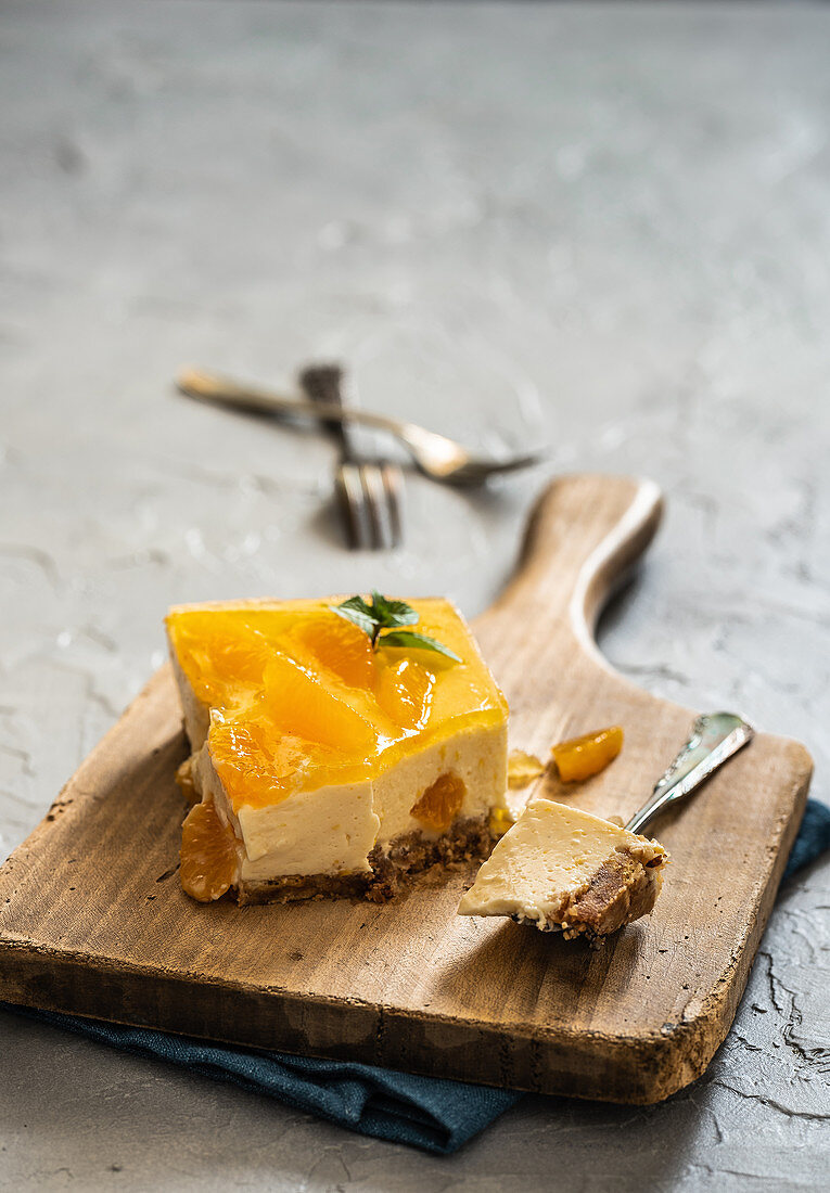 Ein Stück Käsekuchen mit Mandarinen auf Holzbrett