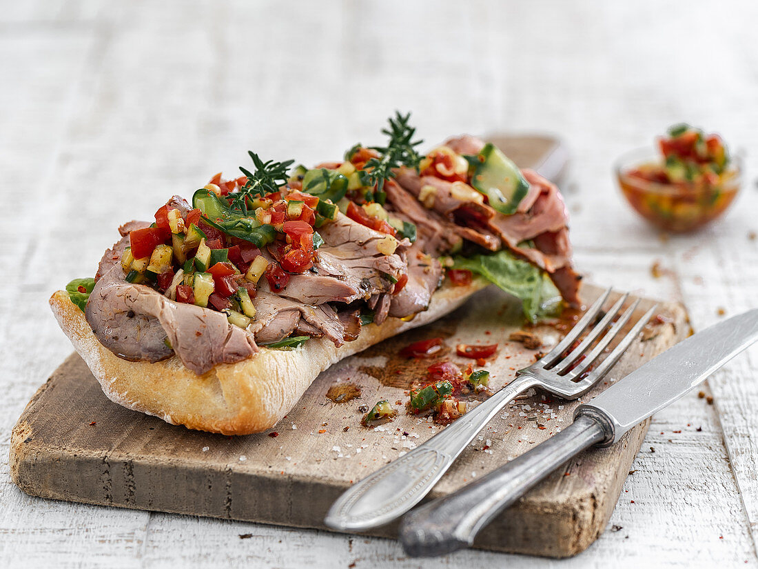 Sandwich rolls with roast beef and bell pepper-zucchini salsa on a wooden board
