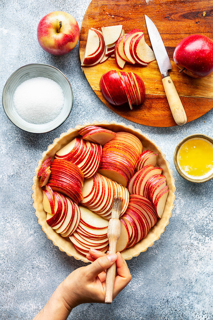 Preparation of an apple tart: Hand brushing sliced apples with melted butter