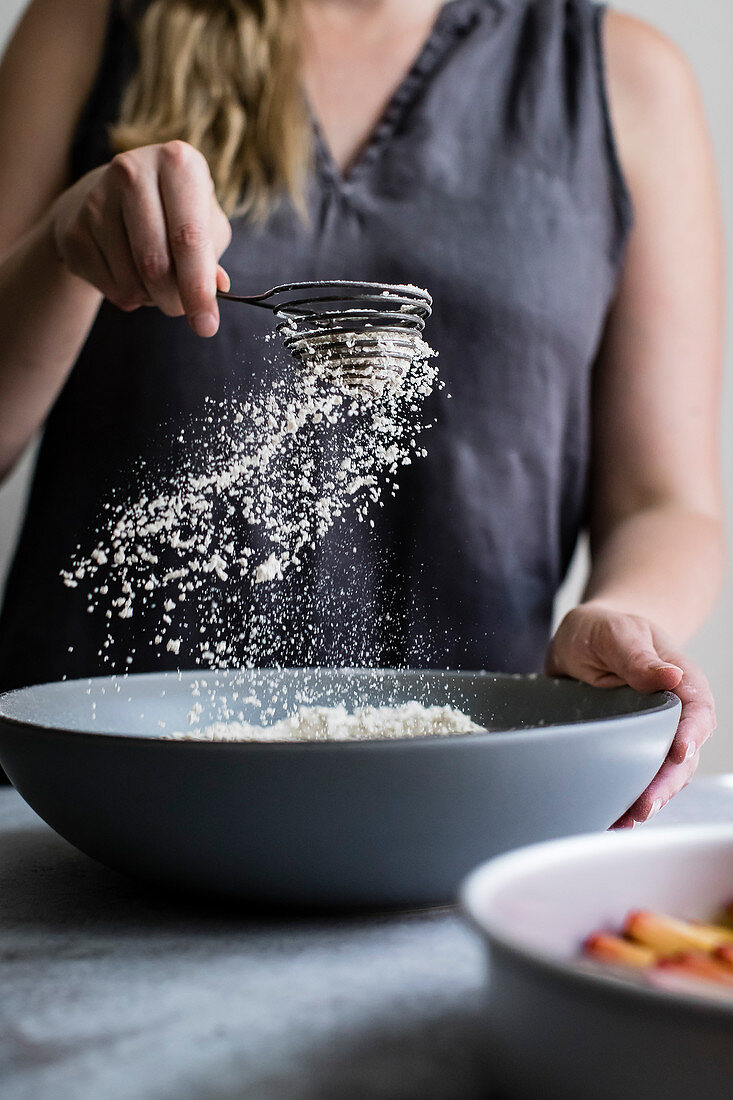 A woman seiving flower over a mixing bowl