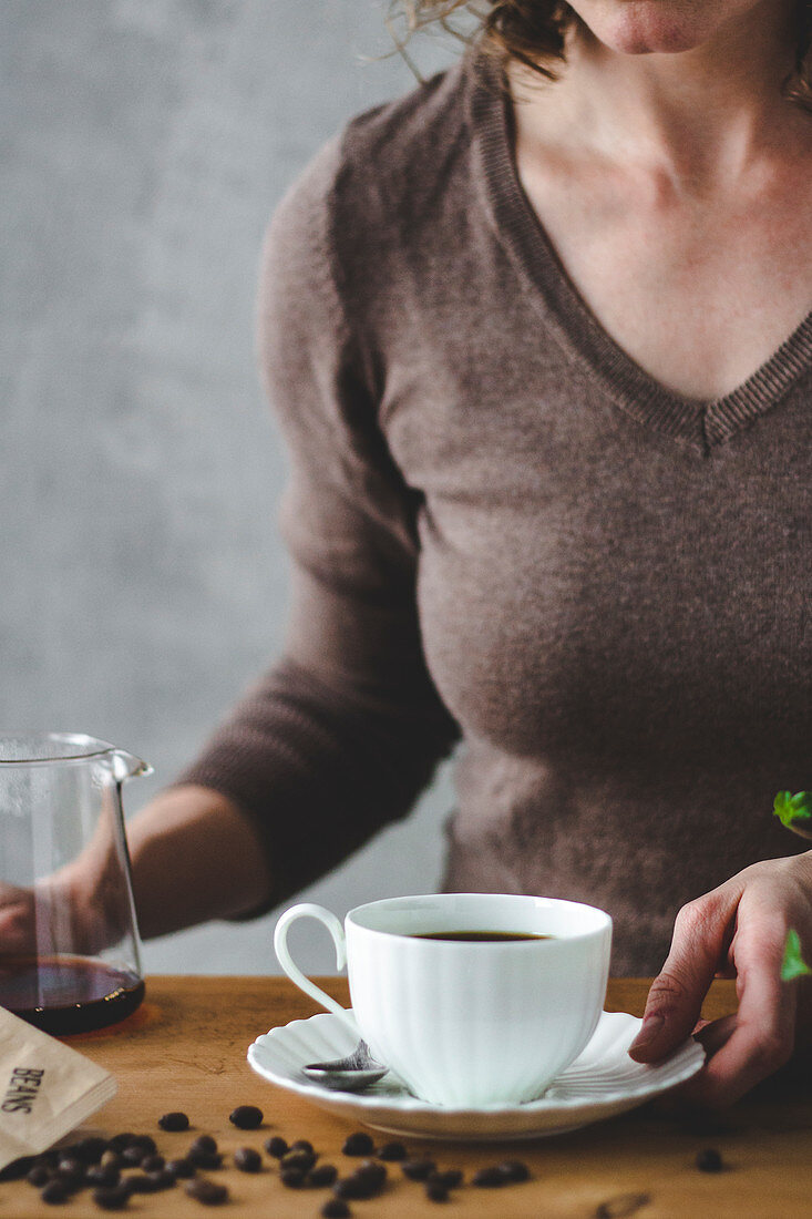 Frau mit Kaffeetasse, Glaskanne und Kaffeebohnen