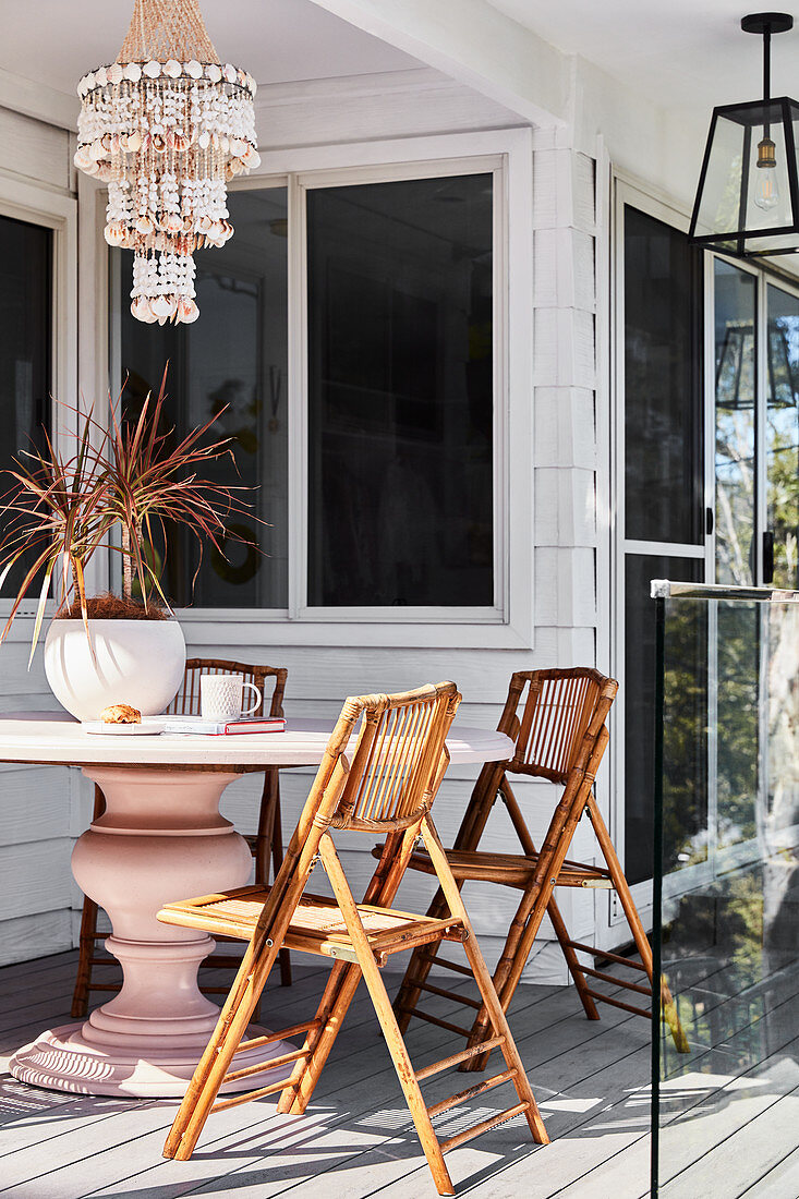 Klappstühle aus Rattan am rosafarbenen Balustertisch auf der Terrasse