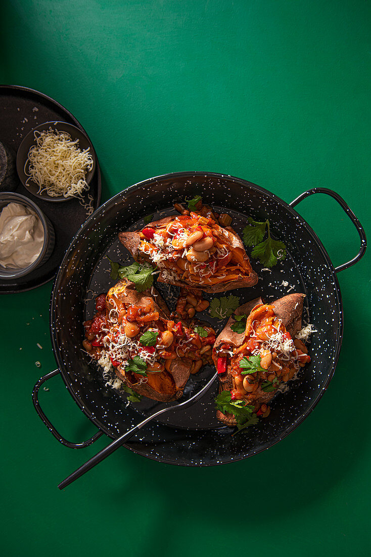 Chipotle bean chilli with baked sweet potatoes, grated cheese, coriander and sour cream