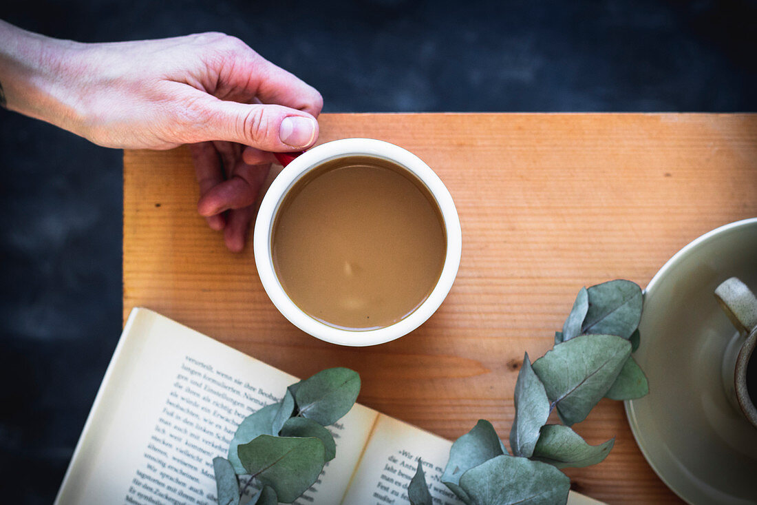 Woman's hand holding a coffee cup on a wooden table with a book