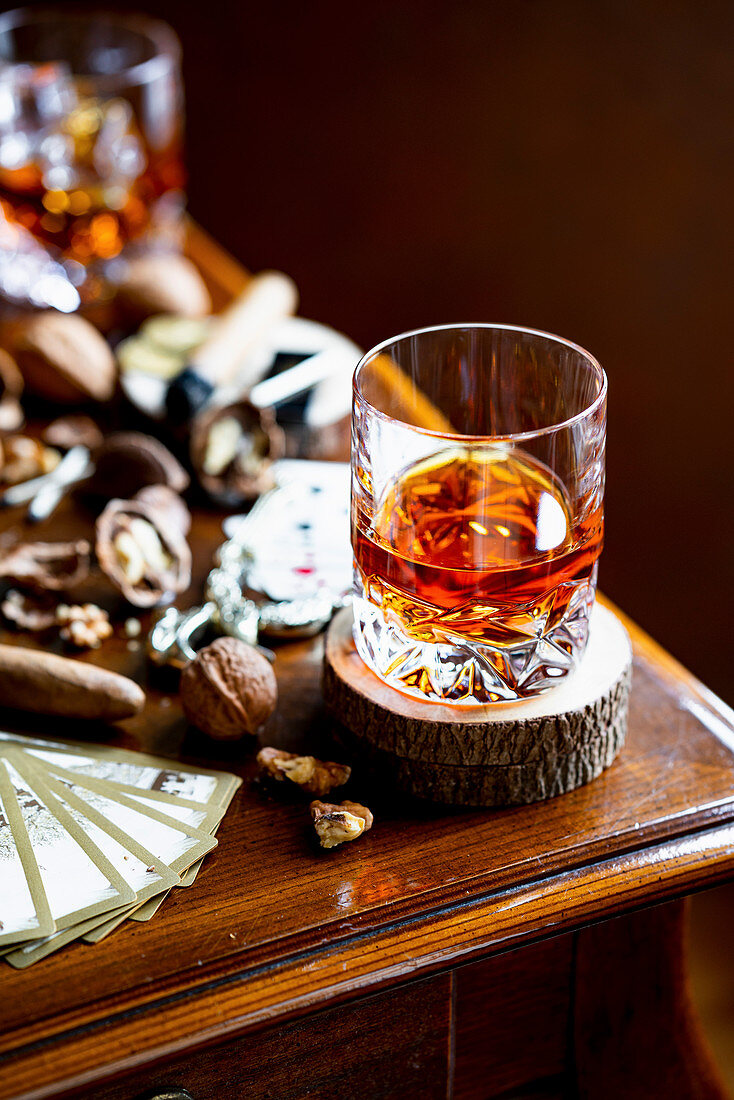 A glass of whiskey next to it, cigar, nuts and playing cards