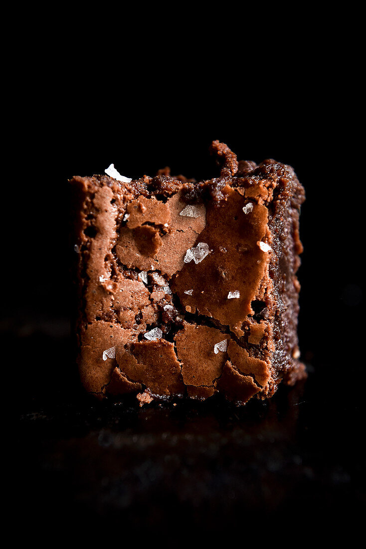 A brownie with flakes of sea salt against a black background