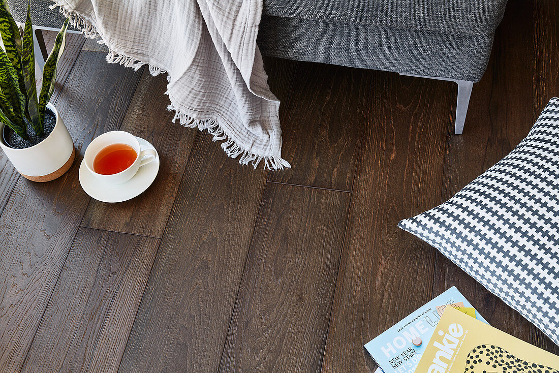 Teacup, blanket, cushion and magazines on dark wooden floor