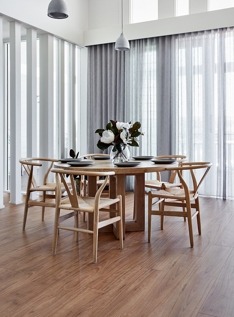 Designer chairs at round wooden table surrounded by glass walls with translucent curtains