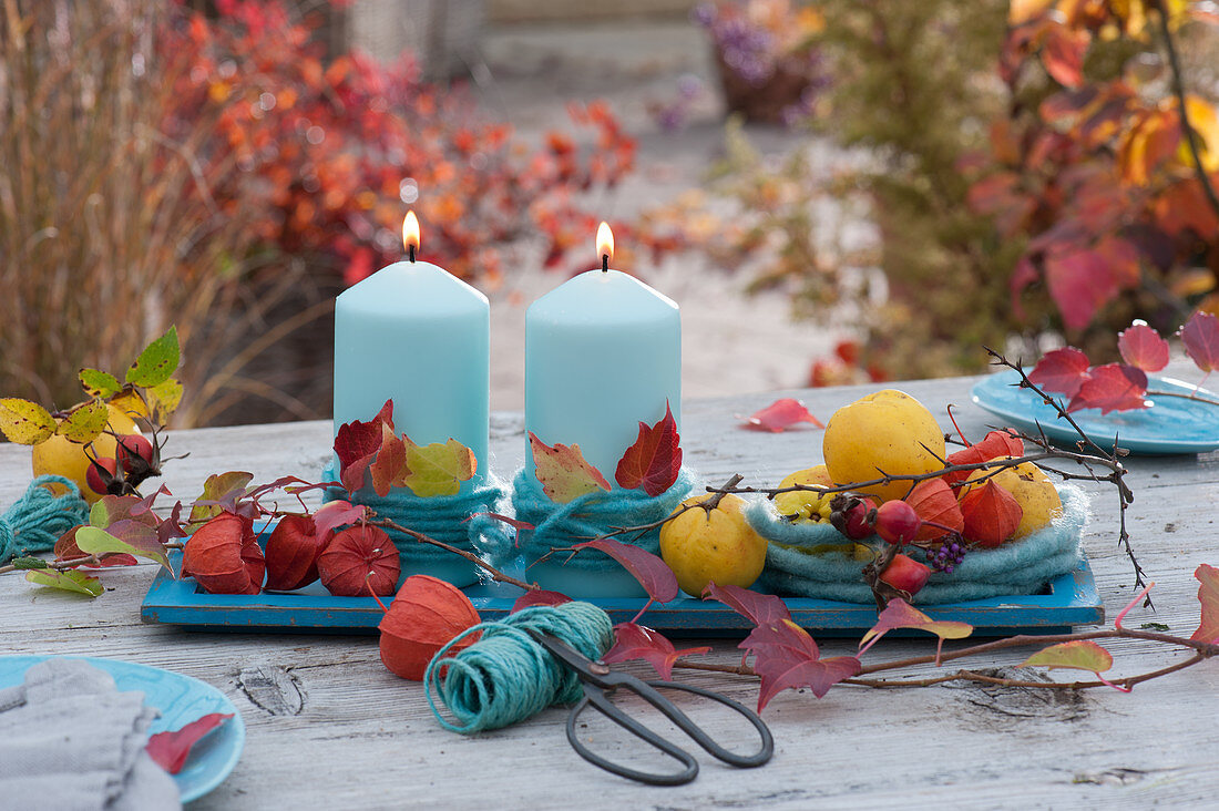 Autumn table setting with turquoise candles, woolen cord, lanterns and decorative quinces