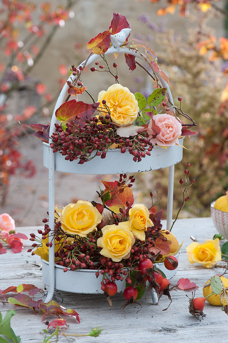 Etagere mit Rosenblüten, Hagebutten und Herbstlaub als Tischdekoration