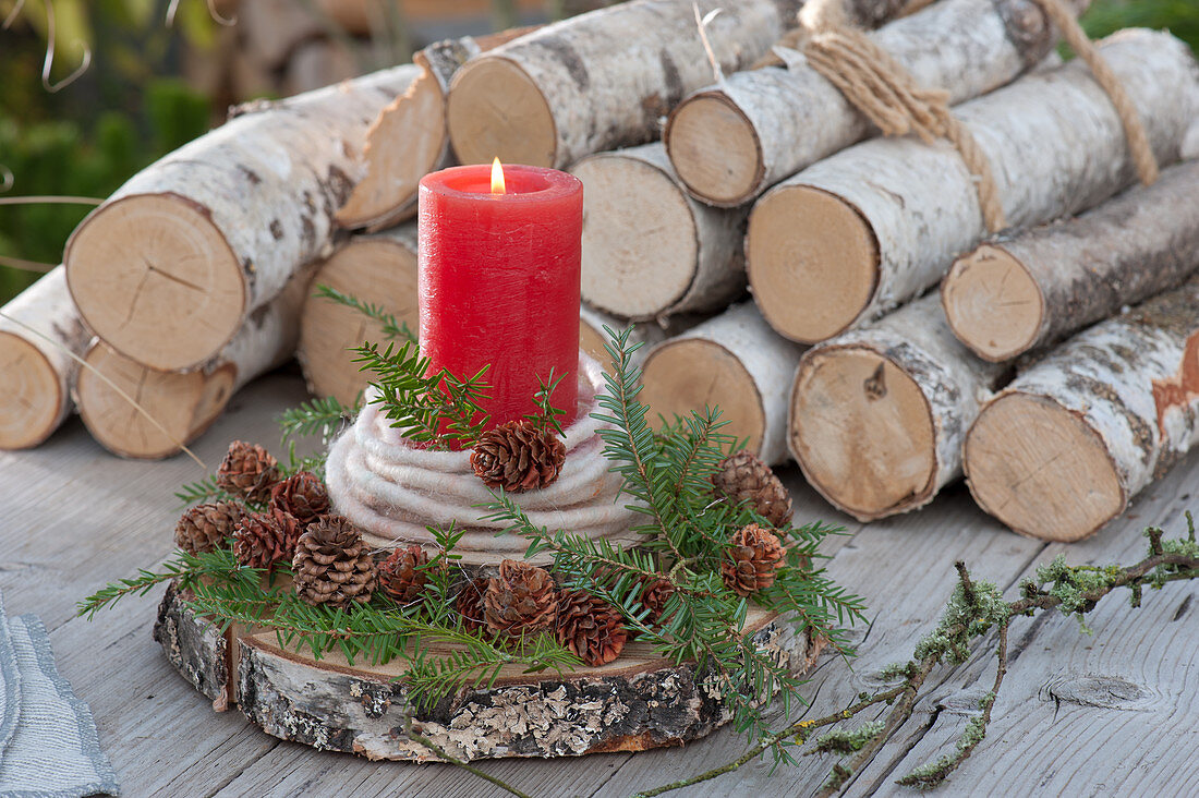 Natürliche Kerzendekoration auf Holzscheibe, dekoriert mit Wollschnur und Zweigen und Zapfen von Hemlocktanne