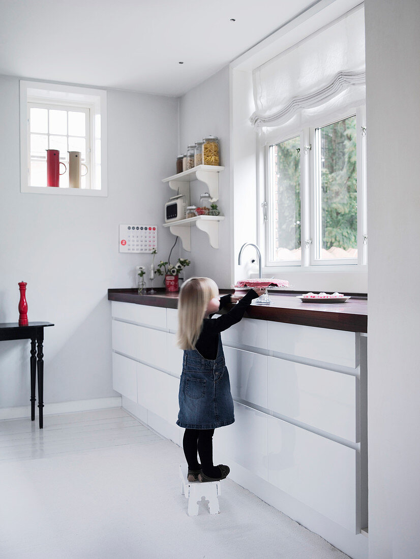 Girl stood on stool in modern kitchen with white floor