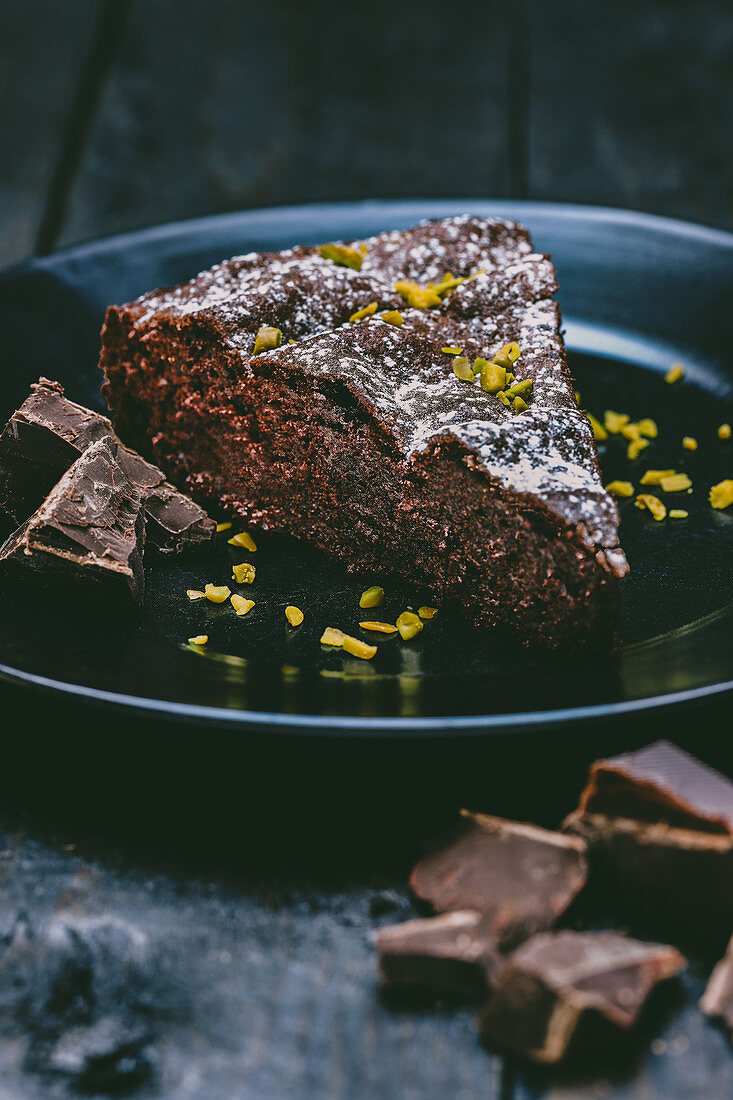A slice of chocolate cake with icing sugar and pistachio nuts