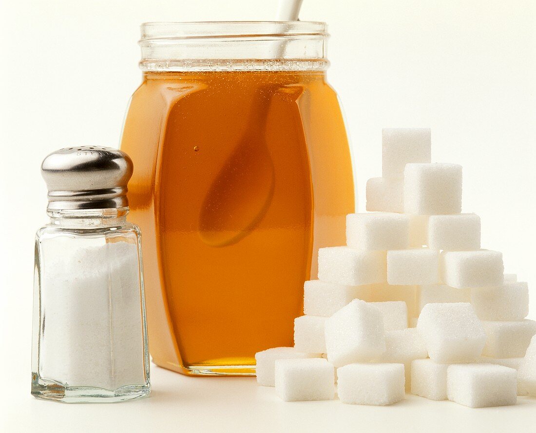 Sugar lumps, honey in jar and icing sugar in sifter