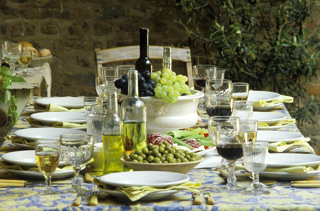 Gedeckter Tisch mit Oliven, Öl & Wein als Tischdeko (außen)