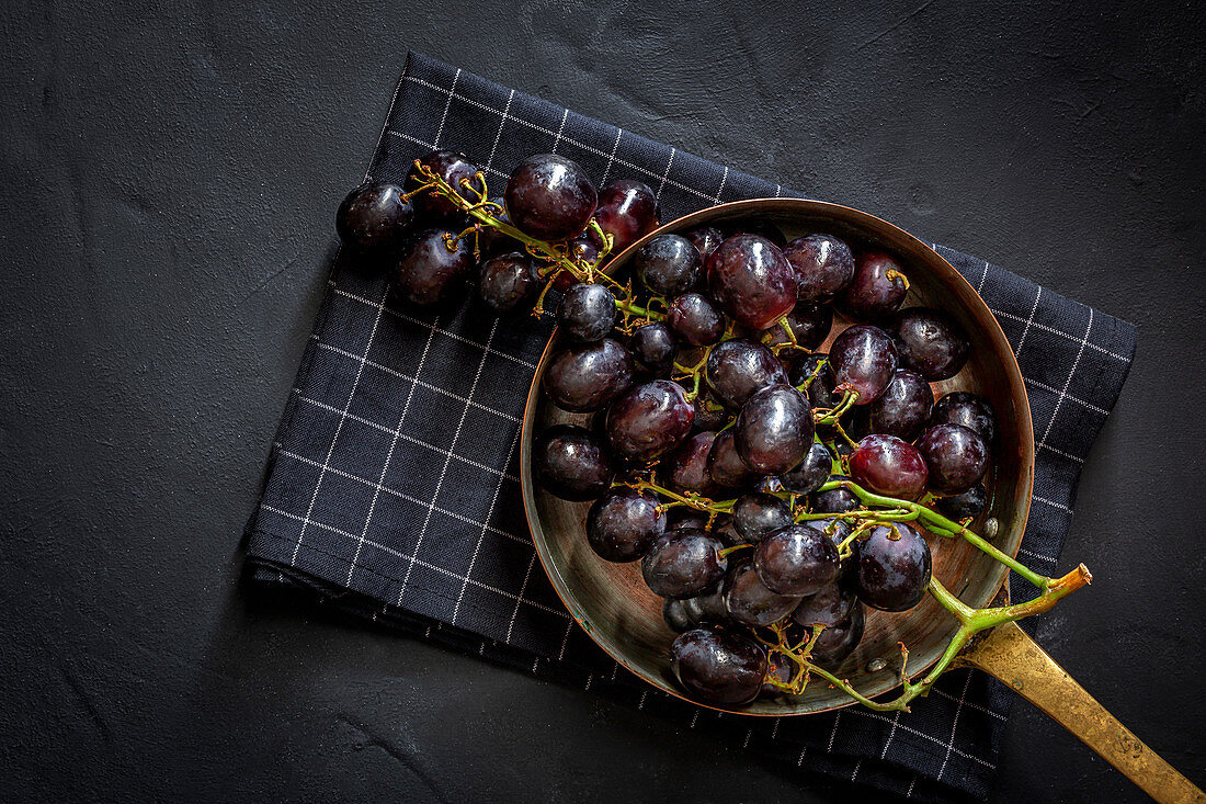 Bunch of delicious sweet ripe red grapes in bowl placed on checkered napkin on black surface