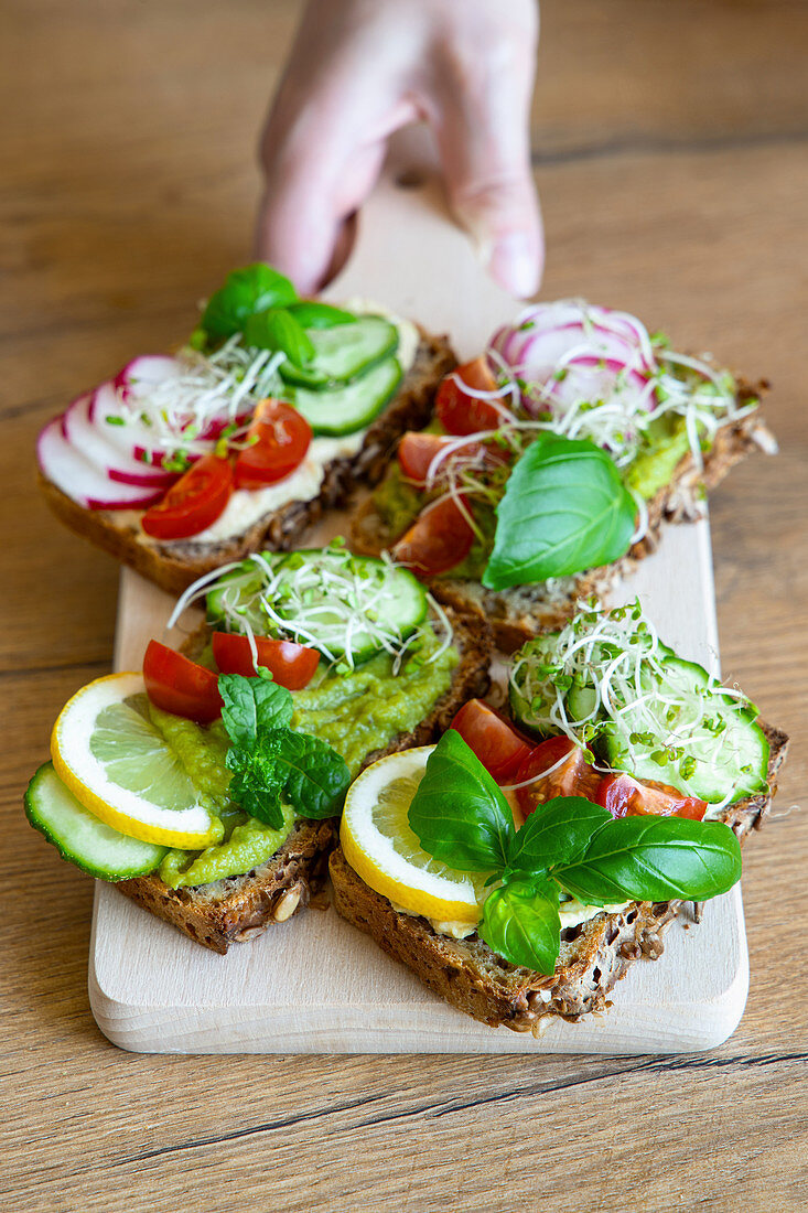 Crop female with delicious toasts with cucumbers and tomatoes garnished with fresh lemon and sprigs of basil