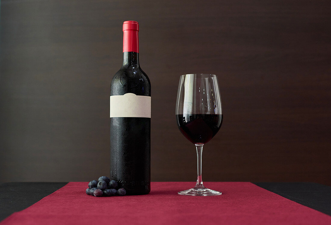 Glass of red wine and bottle placed on table with grapes in luxury restaurant