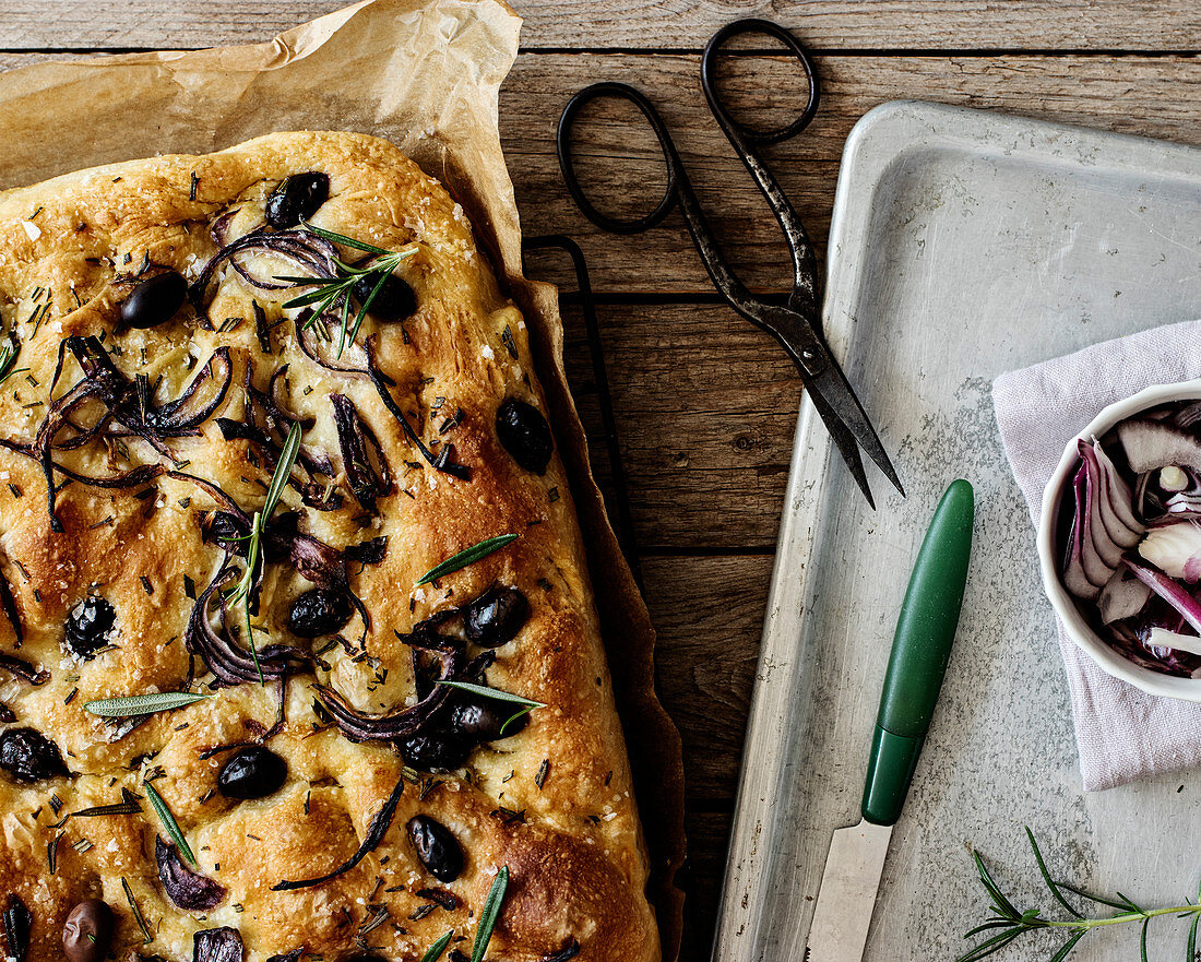 Focaccia with black olives and herbs on wooden table