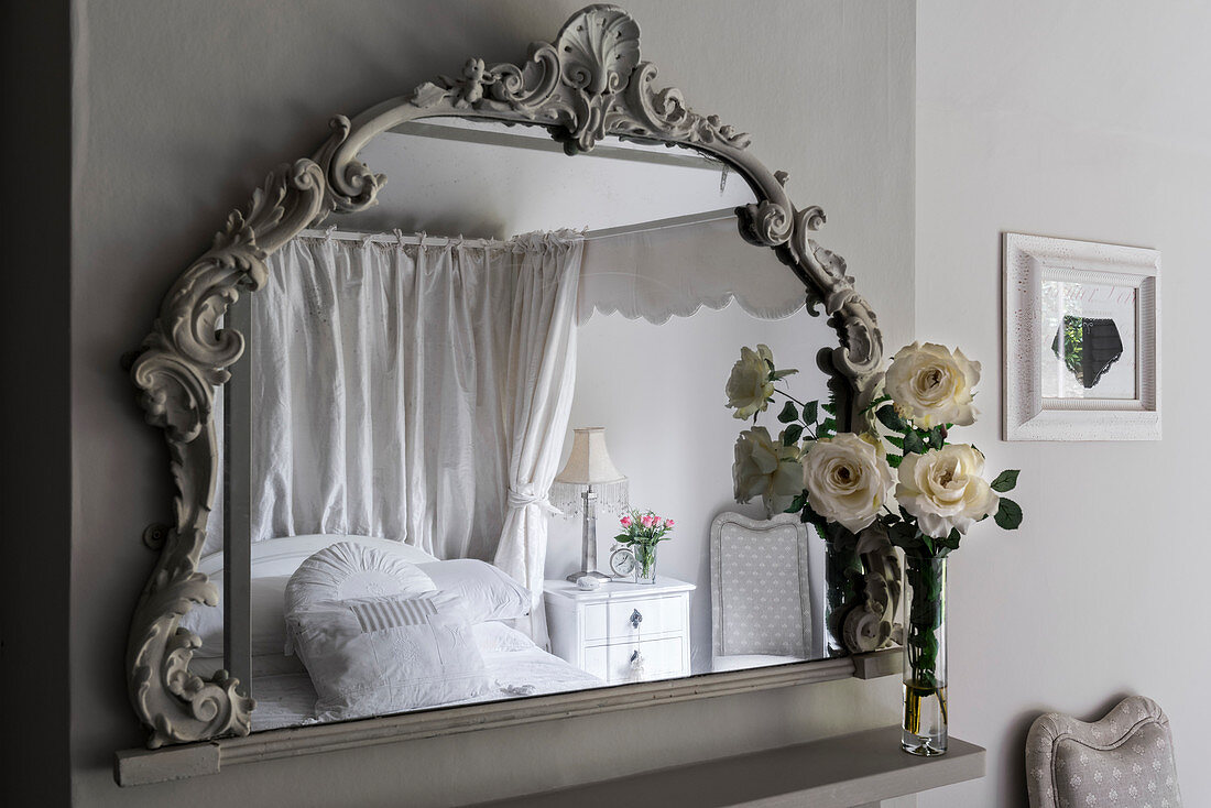 Kissen auf dem Himmelbett reflektiert im Spiegel mit geschnitztem Rahmen und weißen Rosen