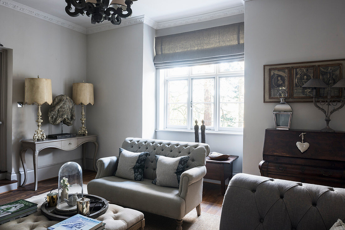 Buttoned sofa at sunlit window with lamps and sculpture on console