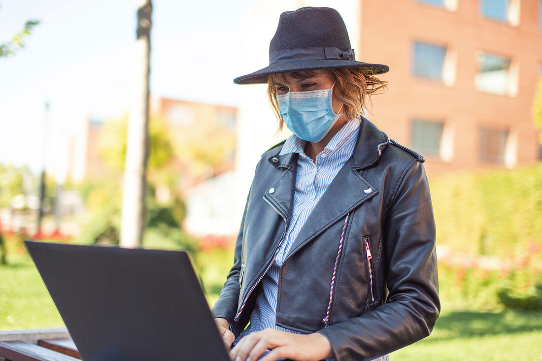 Woman in face mask using laptop in park