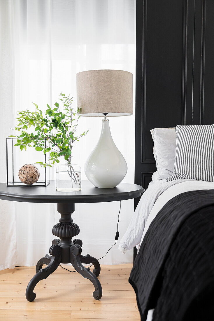 Round, antique bedside table with table lamp and leafy branches